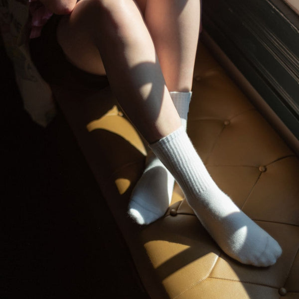 Dame sitzt auf brauner Lederfensterbank, Beine sind überkreuzt, sie trägt unsere weißen Tennissocken.
